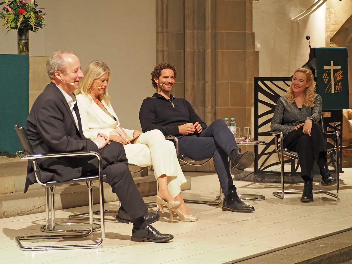 Vier Personen auf Bühne im Gespräch, lächelnd.