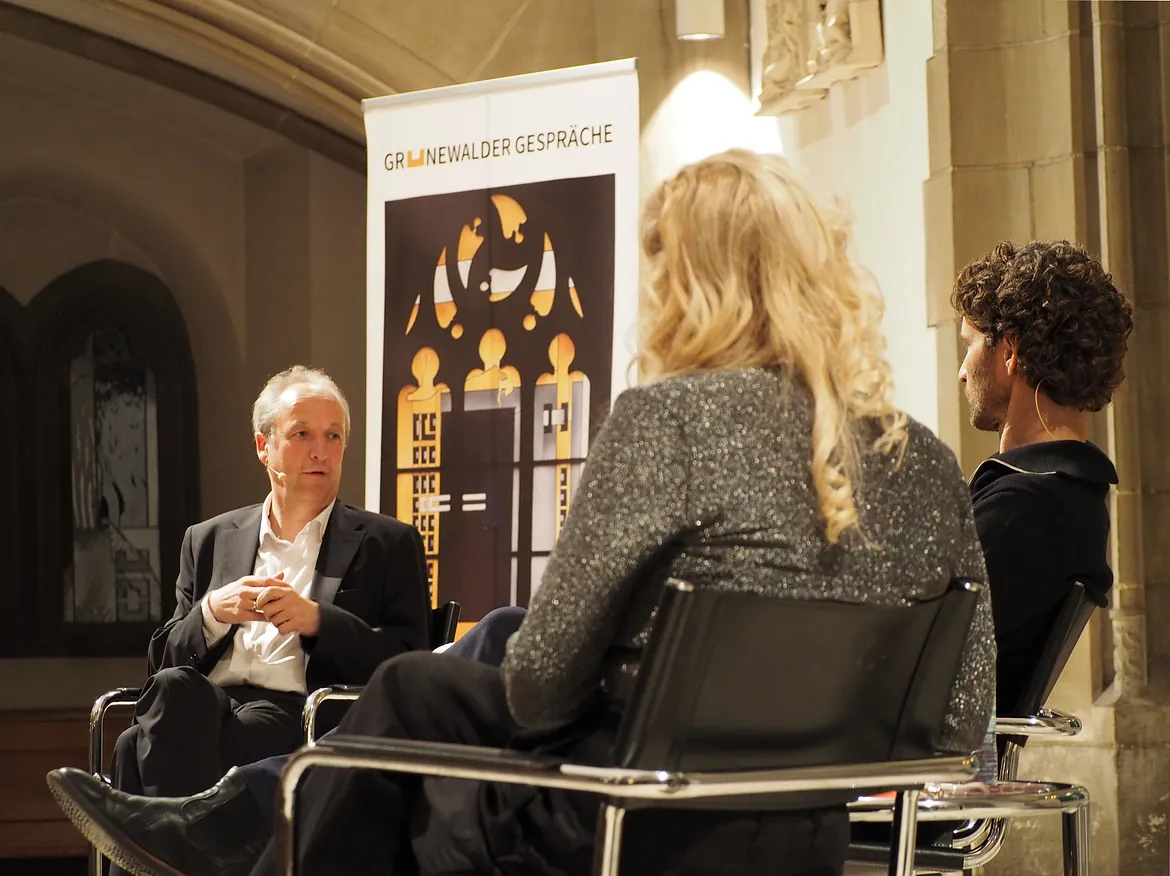 Zwei Personen auf Bühne, Banner im Hintergrund.